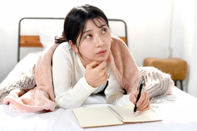 ベッドの上でメモを書く女性